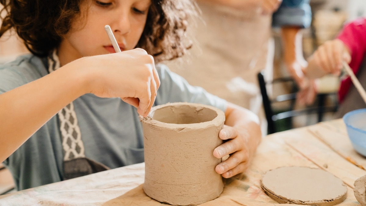 child hand-building a cylindrical clay pot