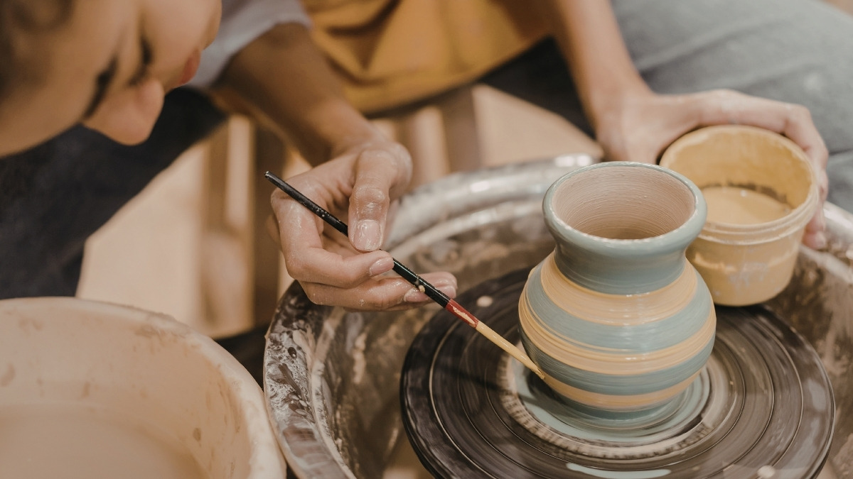 using a slender paintbrush to apply decorative rings of underglaze or slip onto a rotating ceramic vase