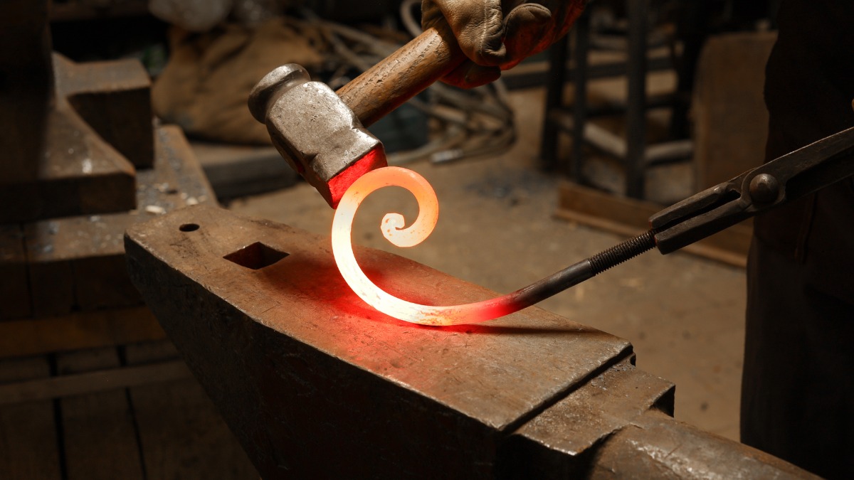 Hammer hitting glowing iron scroll.