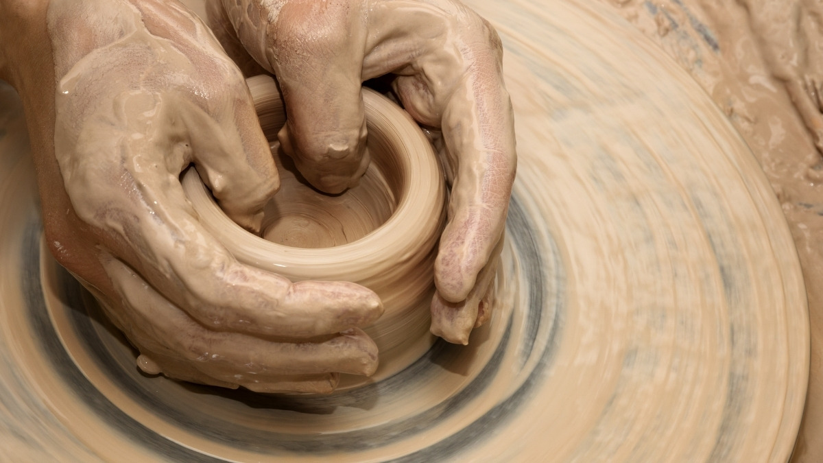 pair of hands shaping wet clay on a spinning pottery wheel