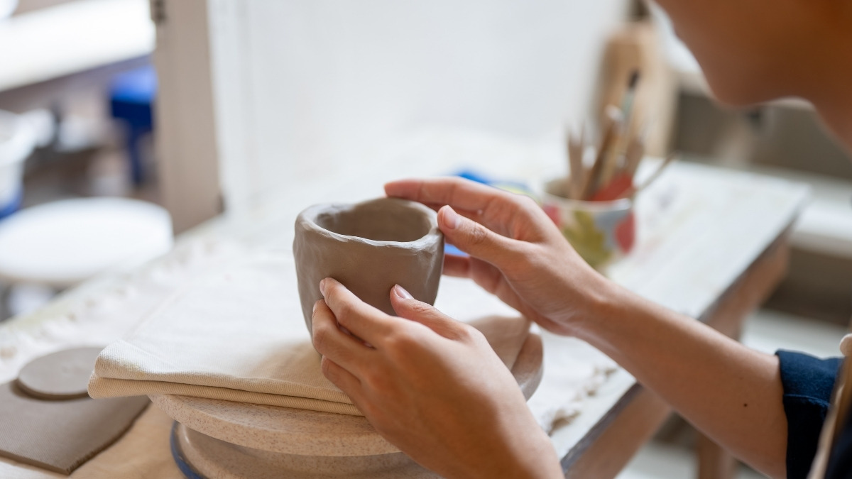 hands-on shaping a small, unglazed clay pot