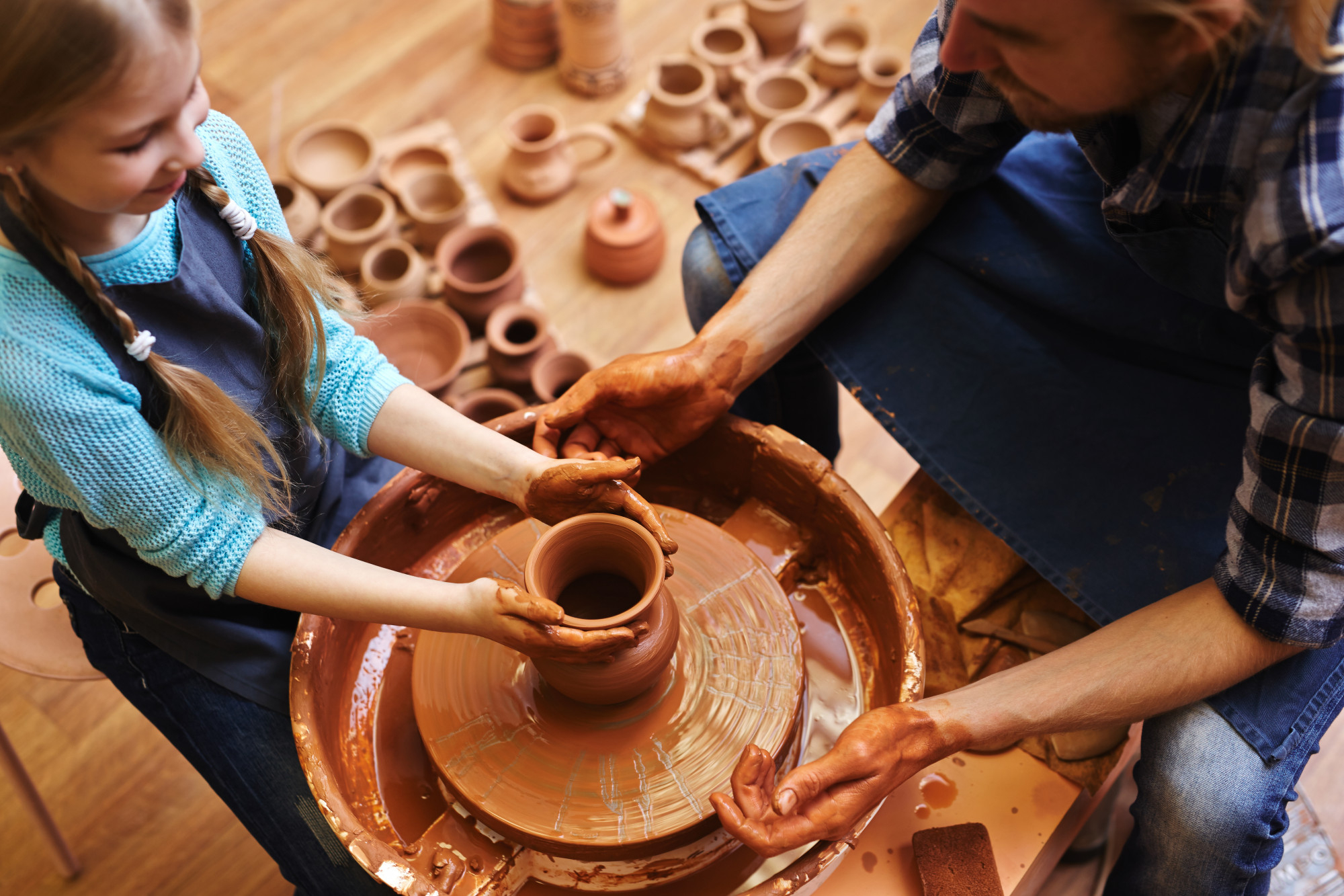 an instructor guiding a young girl's clay-covered hands